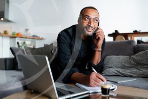 Man concentrating on a phone call while taking notes at a des